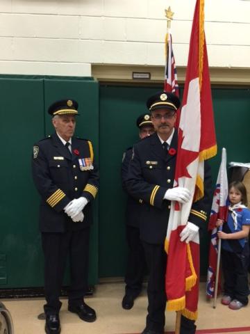 Uniformed men hold a Canadian flag indoors, standing solemnly.