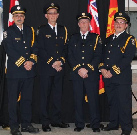 Four uniformed men standing in front of flags, posing for a photo.